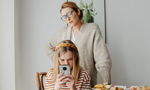 Girl-using-phone-and-her-mom-standing-behind