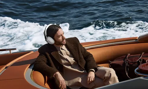A man wearing white Sony 1000X The Collexion over-ear headphones while reclining in a luxury wooden boat on open water.