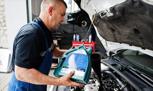 A mechanic in a uniform pouring motor oil into a car engine.