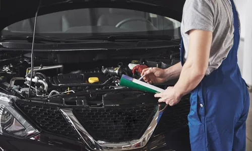 A mechanic inspecting the engine of a car while taking notes.