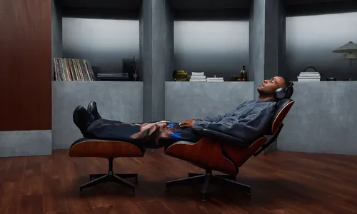Man reclining in an Eames chair wearing Sony 1000X Collexion headphones.