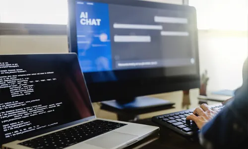 Hand of a Person using AI Chat and Coding application on a laptop and computer