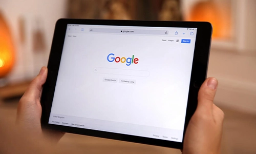 Person holding a tablet displaying the Google search engine homepage