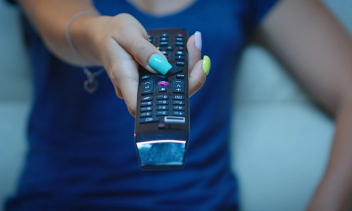 Close-up of woman hand pointing tv remote to change channels sitting in couch to watch television
