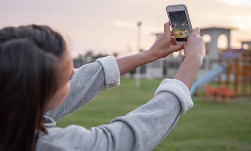 Woman takes a photo of the sky at sunset on her mobile phone.